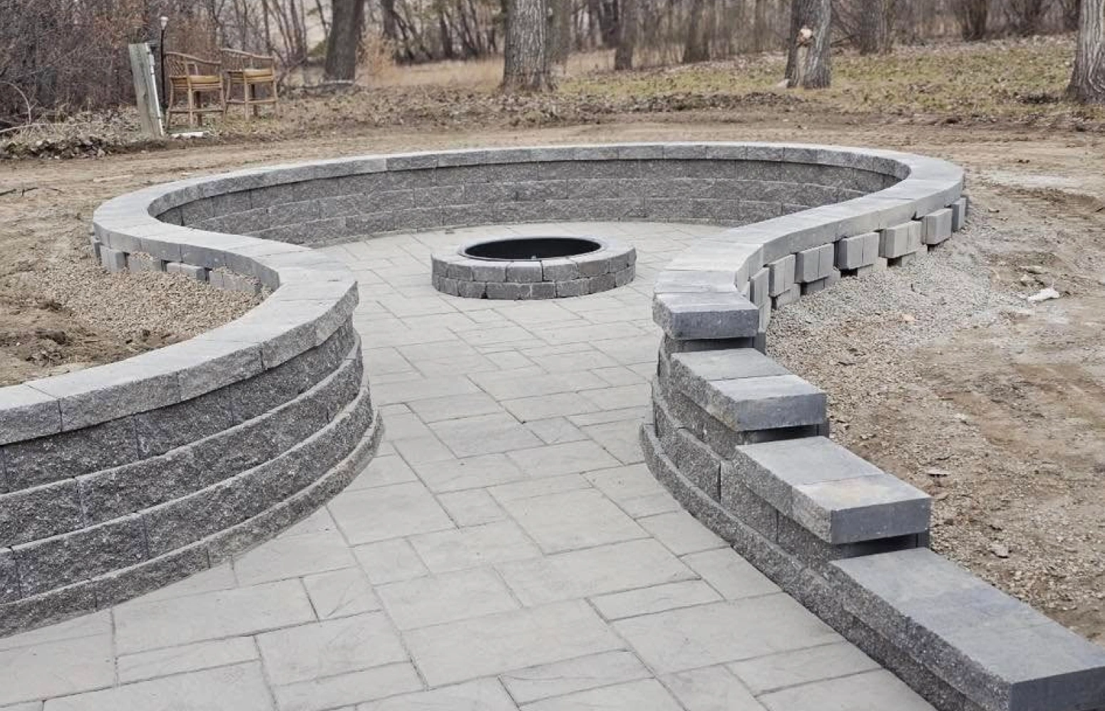 A newly installed gray paver patio with a built in fire pit and a low retaining wall serving as seating. A newly installed gray paver patio with a built in fire pit and a low retaining wall serving as seating.